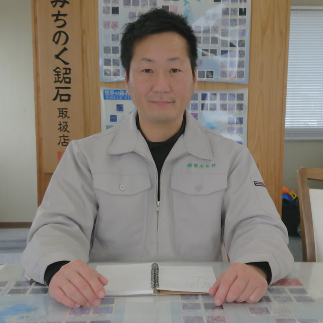 作業服姿の筒木社長が事務所の机で正面を向いて座っている写真